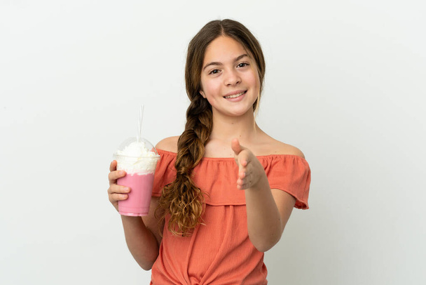 Маленька біла дівчинка з полуничним молочним коктейлем ізольована на білому тлі, тремтячи руками за закриття багато угоди
 - Фото, зображення