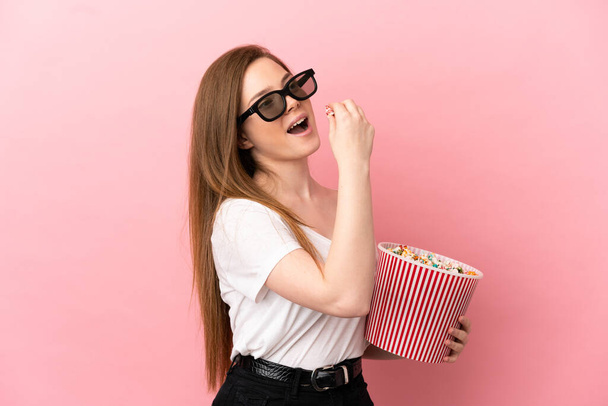 Teenager κορίτσι πάνω από απομονωμένο ροζ φόντο με 3d γυαλιά και κρατώντας ένα μεγάλο κουβά ποπ κορν - Φωτογραφία, εικόνα