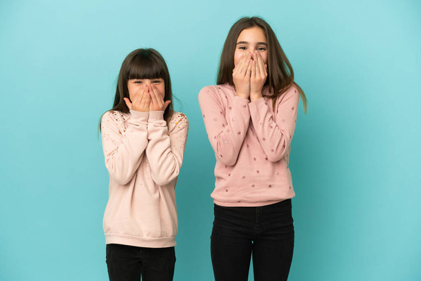Młodsze siostry dziewczyny odizolowane na niebieskim tle uśmiechające się dużo podczas zakrywania ust - Zdjęcie, obraz