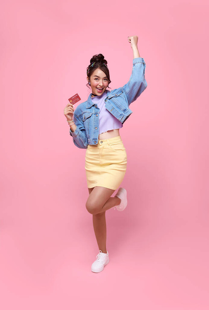 Happy beautiful Asian teen shopaholic women showing credit card in hand isolated on pink background. - Foto, immagini