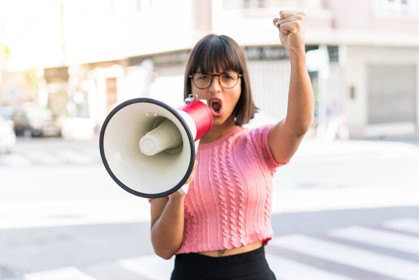 Young brunette woman in the city shouting through a megaphone to announce something - Foto, Imagem