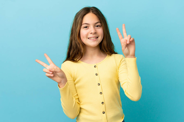 Pequeña chica caucásica aislada sobre fondo azul mostrando signo de victoria con ambas manos - Foto, Imagen