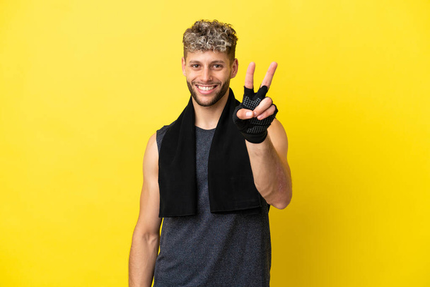 Sport caucasian man isolated on yellow background smiling and showing victory sign - Foto, Imagen