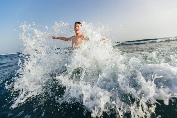 Счастливый ребенок, играющий в море. Ребенок веселится на улице. Летние каникулы и здоровый образ жизни. Селективный фокус - Фото, изображение