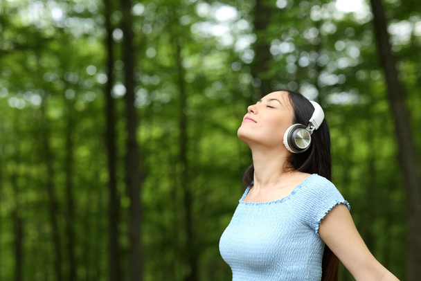 Asian woman listening to music wearing headphones breathing fresh air in a forest - Фото, изображение