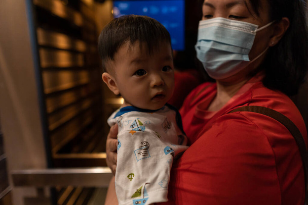 mignon et adorable asiatique chinois bébé garçon porter jusqu 'par mère avec médical visage masque pendant à l' extérieur pour protéger contre coronavirus infection - Photo, image