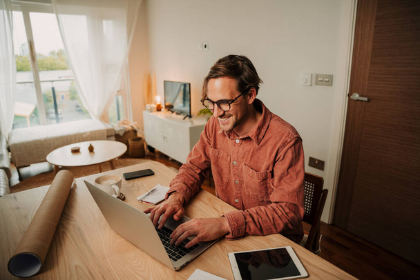 Caucásico estudiante masculino escribiendo en el ordenador portátil de trabajo en el escritorio de casa configurado  - Foto, Imagen