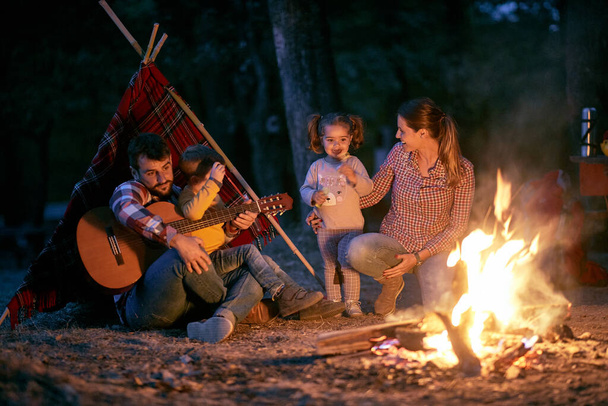 A young couple and children around a campfire in the forest in a beautiful night - Photo, Image