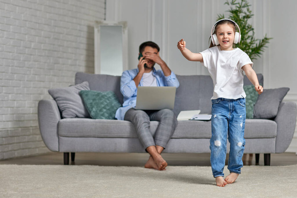 kid dancing and busy dad working with laptop at home - Foto, Imagen