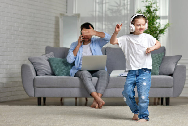 kid dancing and busy dad working with laptop at home - Foto, imagen