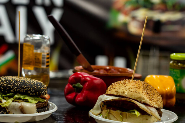 Dos hamburguesas de queso en una mesa con pimientos rojos y amarillos en el fondo en el mostrador de comida de la calle - Foto, imagen