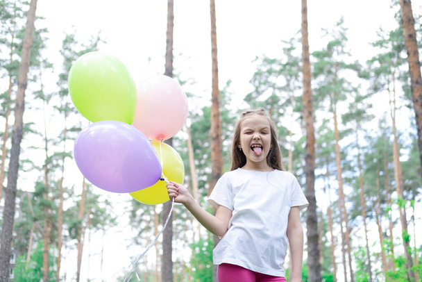 красива дівчина дошкільного віку розважається, граючи з повітряними кулями на відкритому повітрі. Холлідейс, вечірка, день народження, свято. щасливі діти
.  - Фото, зображення