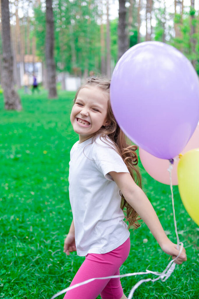 красива дівчина дошкільного віку розважається, граючи з повітряними кулями на відкритому повітрі. Холлідейс, вечірка, день народження, свято. щасливі діти
.  - Фото, зображення