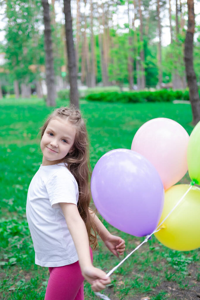 όμορφο κορίτσι προσχολικής ηλικίας που διασκεδάζει παίζοντας με αερόστατα θερμού αέρα σε εξωτερικούς χώρους. Χόλιντεϊ, πάρτι, γενέθλια, γιορτή. ευτυχισμένα παιδιά.  - Φωτογραφία, εικόνα