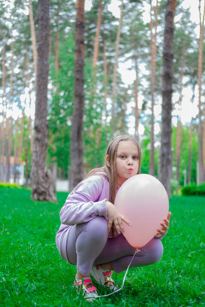 όμορφη κοπέλα μεταξύ έφηβος σε μωβ κοστούμι διασκεδάζοντας παίζοντας με ζεστό αέρα ροζ μπαλόνι σε εξωτερικούς χώρους. Χόλιντεϊ, πάρτι, γενέθλια, γιορτή. ευτυχισμένα παιδιά. - Φωτογραφία, εικόνα