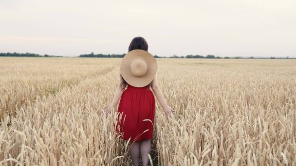A free girl in a red dress runs cheerfully across a wheat field in open air. A woman farmer touches the ears of wheat with her hands. Travel in the countryside. Happy free girl runs across the field. - Fotó, kép