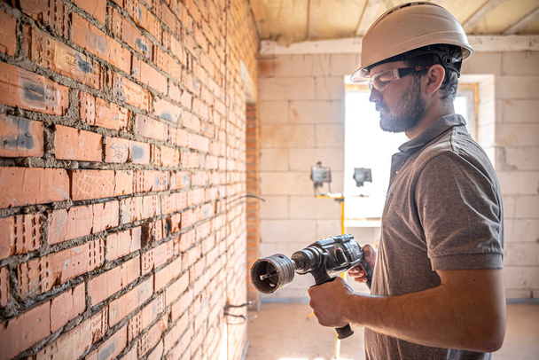 Homme à tout faire sur un chantier en train de percer un mur avec une perforatrice. - Photo, image