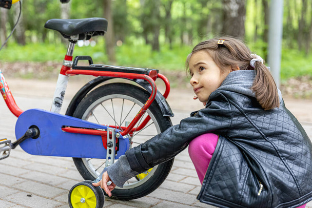 Egy kislány sétál a parkban a biciklijével.. - Fotó, kép