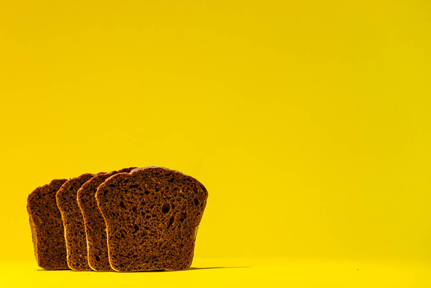 QUATRO fatias de pão preto sourdough ficar lado a lado contra um fundo amarelo brilhante. - Foto, Imagem