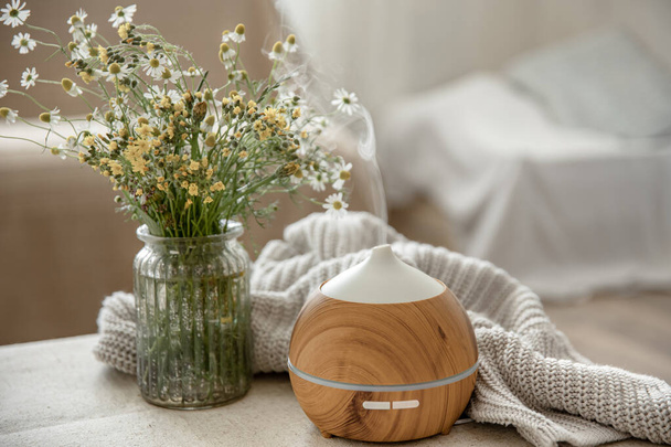 Moderní olej aroma difuzor v obývacím pokoji na stole s pleteným prvkem a květy. - Fotografie, Obrázek