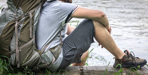 Un turista con un grande zaino si sedette a riposare vicino al fiume. - Foto, immagini