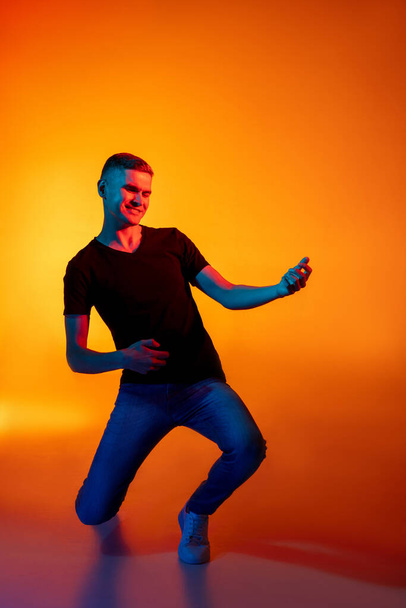 Portret van de jonge blanke man in casual kleding geïsoleerd over gradiënt rood oranje studio achtergrond in neon licht met copyspace voor reclame. Concept van menselijke emoties - Foto, afbeelding