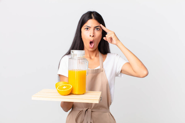pretty hispanic chef woman looking surprised, realizing a new thought, idea or concept and holding a orange juice - Foto, Imagem