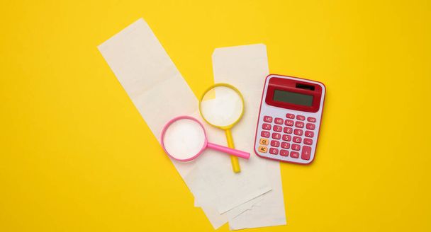 стопка паперових чеків, рожевий пластиковий калькулятор і збільшувальне скло на жовтому тлі. Концепція перевірки сімейного бюджету, пошук заощаджень
 - Фото, зображення