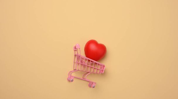 red heart in a miniature metal trolley from the store on a beige  background. Organ donation, transplant concept, top view - Photo, Image