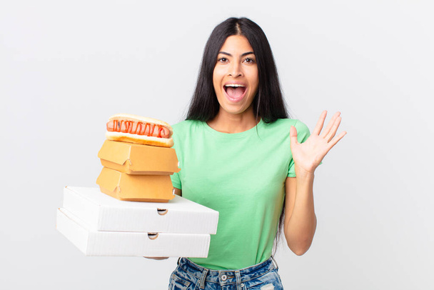 pretty hispanic woman feeling happy and astonished at something unbelievable and holding take away fast food boxes - Zdjęcie, obraz