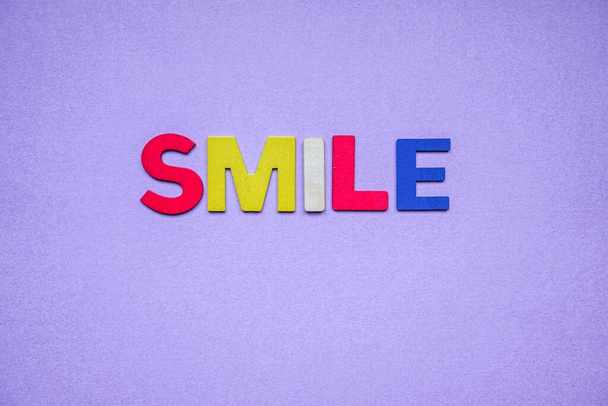 palabra sonrisa con letras de madera sobre el fondo púrpura  - Foto, Imagen