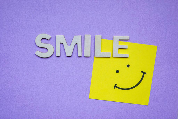 słowo uśmiech z drewnianymi literami na fioletowym tle  - Zdjęcie, obraz