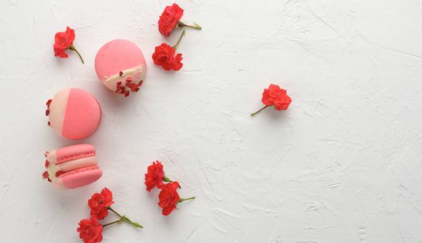 macarons aux fraises rouges cuites au four et boutons de rose sur une table blanche, dessert gourmet à la farine d'amande, vue sur le dessus - Photo, image