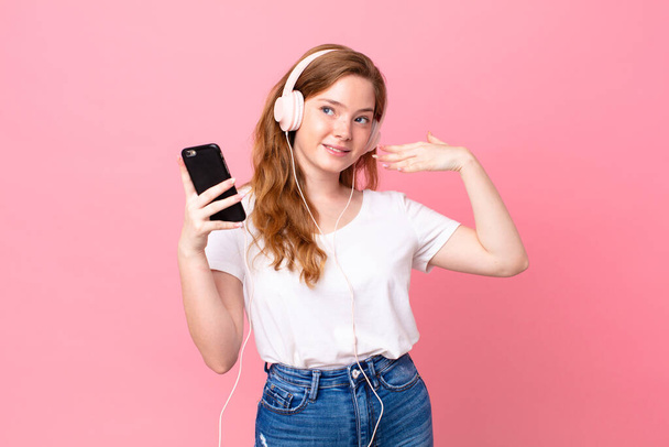 pretty red head woman feeling stressed, anxious, tired and frustrated with headphones and smartphone - Fotoğraf, Görsel