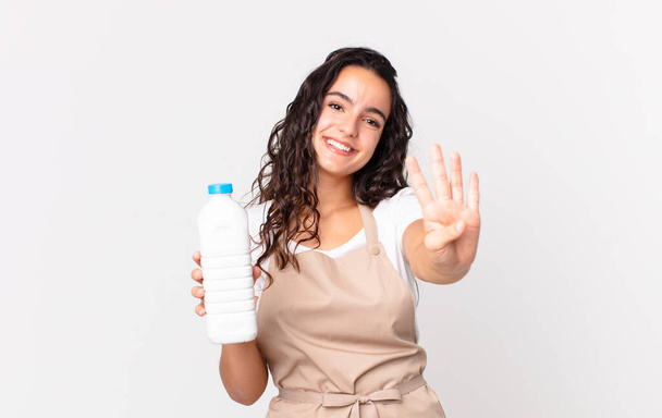 hispanic pretty chef woman smiling and looking friendly, showing number four and holding a milk bottle - Fotoğraf, Görsel