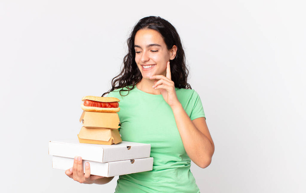 pretty hispanic woman smiling happily and daydreaming or doubting and holding take away fast food boxes - Фото, изображение