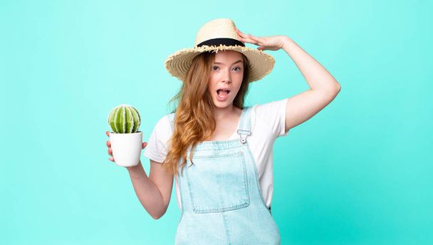 red head pretty farmer woman looking happy, astonished and surprised and holding a cactus - Foto, Imagem