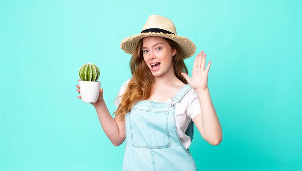 red head pretty farmer woman smiling and looking friendly, showing number five and holding a cactus - 写真・画像