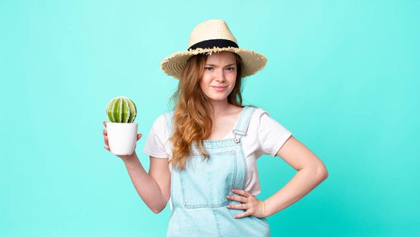 red head pretty farmer woman feeling sad, upset or angry and looking to the side and holding a cactus - Photo, Image