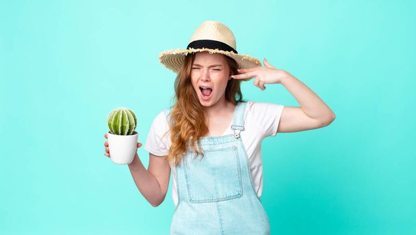 red head pretty farmer woman looking unhappy and stressed, suicide gesture making gun sign and holding a cactus - Photo, image