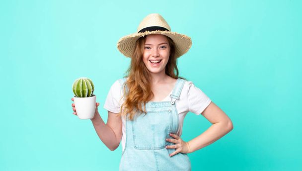 red head pretty farmer woman looking happy and pleasantly surprised and holding a cactus - Foto, Imagen