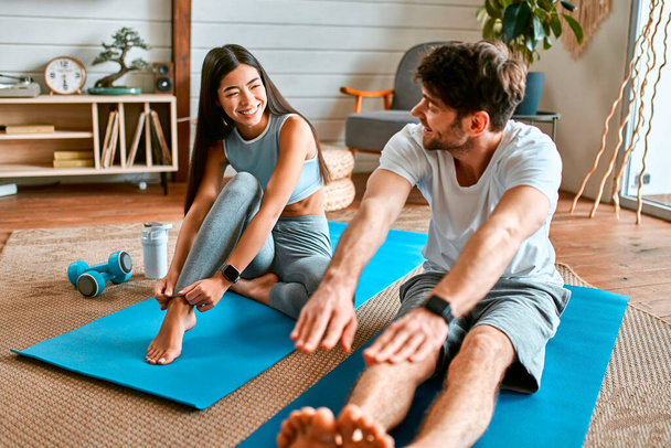 Um jovem casal em sportswear estão fazendo exercícios em esteiras em casa em uma sala de estar acolhedora brilhante. Estilo de vida saudável, esporte, ioga, fitness. - Foto, Imagem