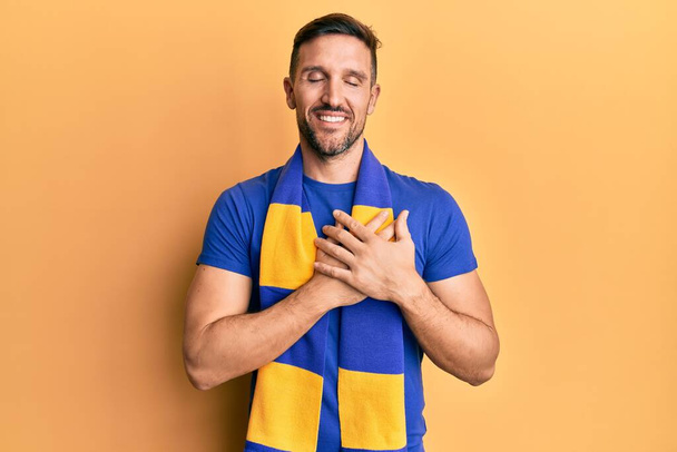 Handsome man with beard football hooligan cheering game smiling with hands on chest, eyes closed with grateful gesture on face. health concept.  - Photo, Image