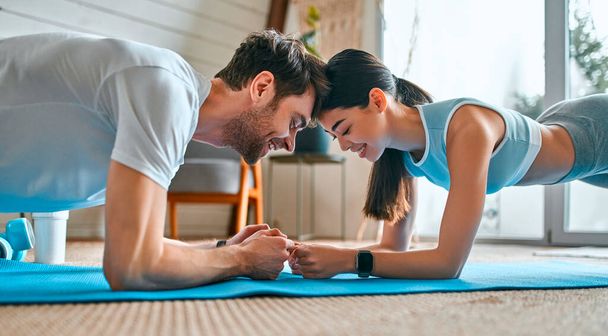 スポーツウェアのかわいいカップルは自宅のリビングルームのマットの上に運動板を行います。健康的なライフスタイル、スポーツ、ヨガ、フィットネス. - 写真・画像