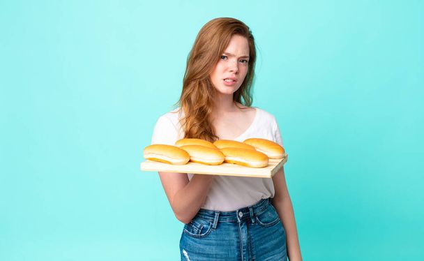 red head pretty woman feeling puzzled and confused and holding a bread buns troy - 写真・画像