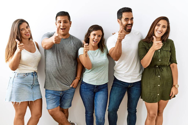Groupe de jeunes amis hispaniques debout ensemble sur fond isolé pointant les doigts vers la caméra avec un visage heureux et drôle. bonne énergie et vibes.  - Photo, image