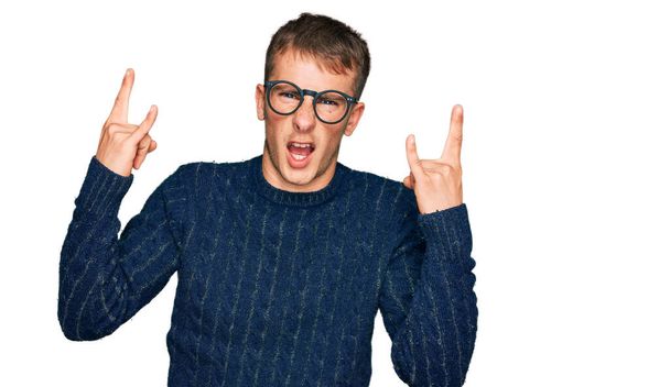 Young blond man wearing casual clothes and glasses shouting with crazy expression doing rock symbol with hands up. music star. heavy concept.  - Photo, Image