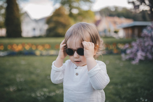 Little boy in sunglasses is walking in the garden. - Zdjęcie, obraz