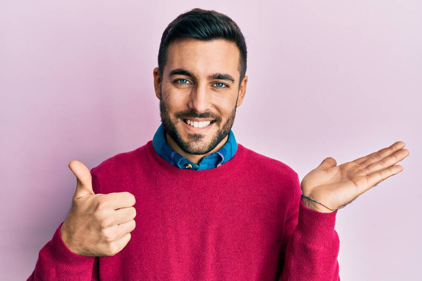 Молодой латиноамериканец в повседневной одежде показывает ладонь и делает все хорошо жесты с большими пальцами вверх, улыбаясь счастливым и веселым  - Фото, изображение