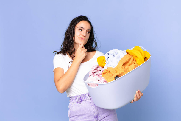 hispanic pretty woman thinking, feeling doubtful and confused and holding a washing clothes basket - Φωτογραφία, εικόνα